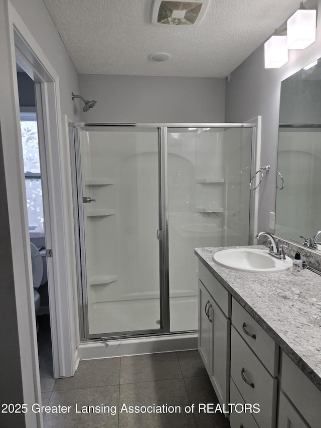 full bath with toilet, a stall shower, a textured ceiling, vanity, and tile patterned floors