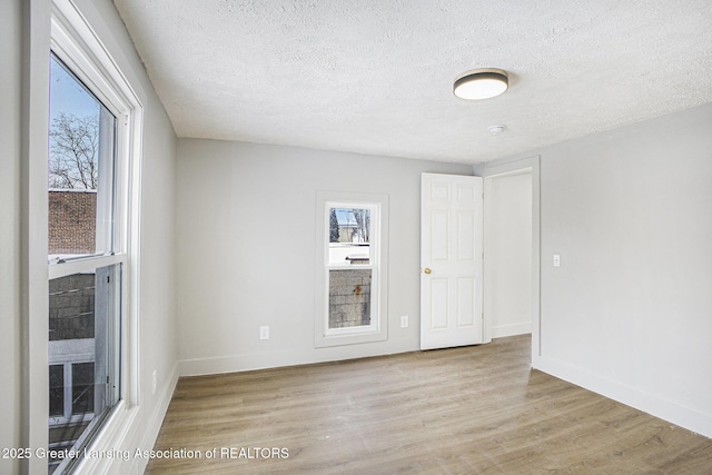 spare room with light wood-style flooring, baseboards, and a textured ceiling