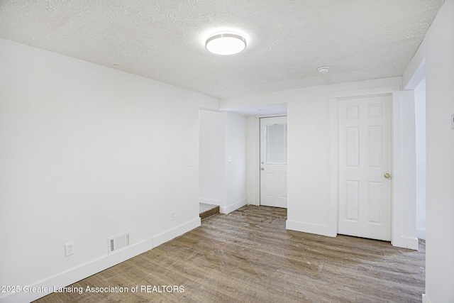 unfurnished bedroom featuring a textured ceiling, wood finished floors, visible vents, and baseboards