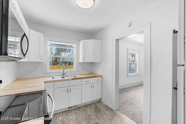 kitchen featuring stainless steel range with electric cooktop, white cabinets, a sink, and wood counters