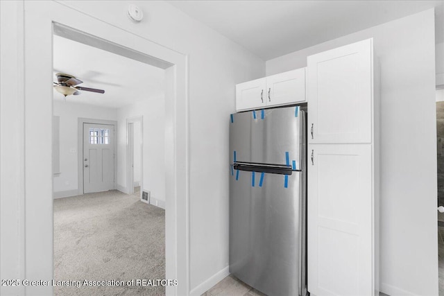 kitchen with light colored carpet, freestanding refrigerator, white cabinetry, and baseboards