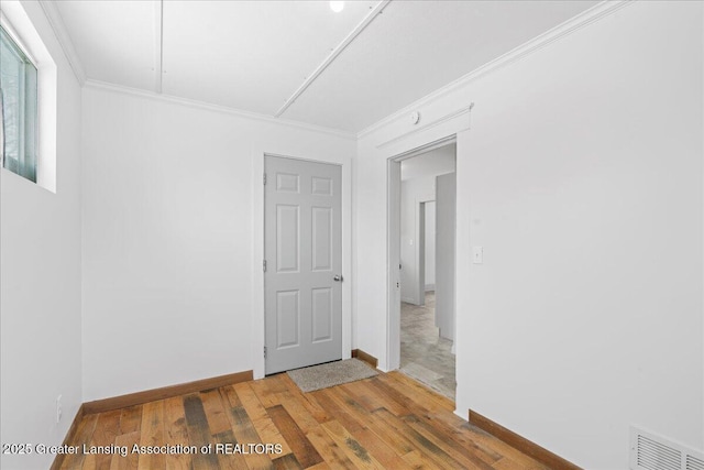 spare room featuring baseboards, wood finished floors, visible vents, and crown molding