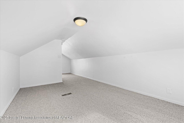 additional living space with vaulted ceiling, light colored carpet, visible vents, and baseboards