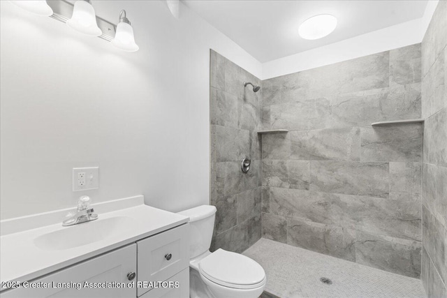 full bathroom featuring tiled shower, vanity, and toilet