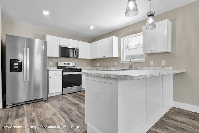 kitchen with hanging light fixtures, appliances with stainless steel finishes, wood finished floors, and white cabinets