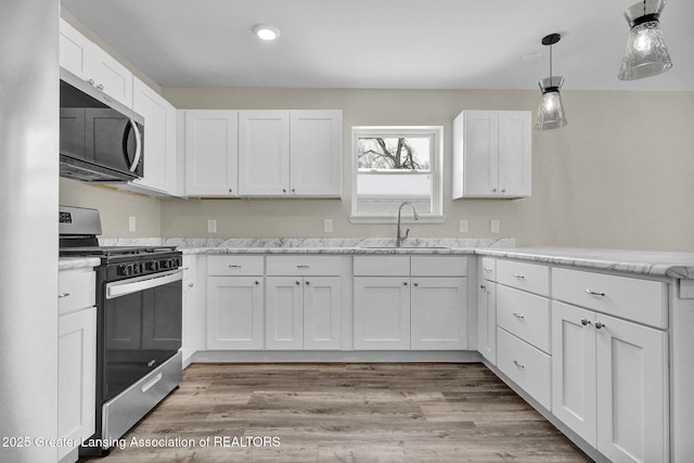 kitchen with light wood-style flooring, stainless steel appliances, white cabinetry, pendant lighting, and a sink