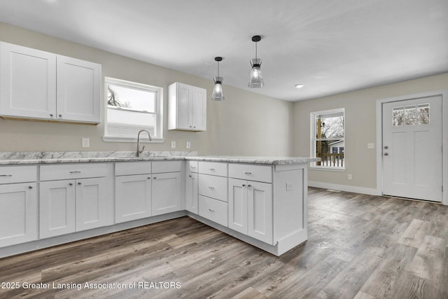 kitchen featuring white cabinets, decorative light fixtures, a peninsula, and wood finished floors