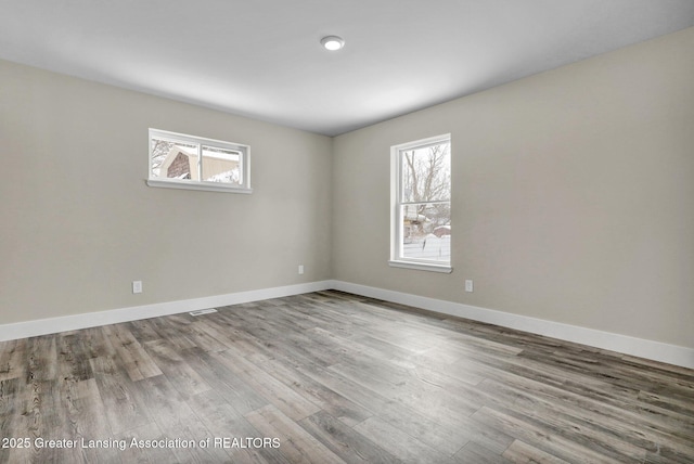 unfurnished room with plenty of natural light, wood finished floors, and baseboards