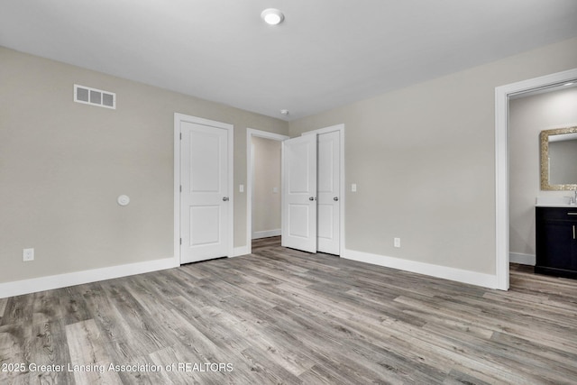 unfurnished bedroom with ensuite bathroom, light wood-type flooring, visible vents, and baseboards