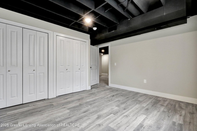 unfurnished bedroom with light wood-type flooring, baseboards, and two closets