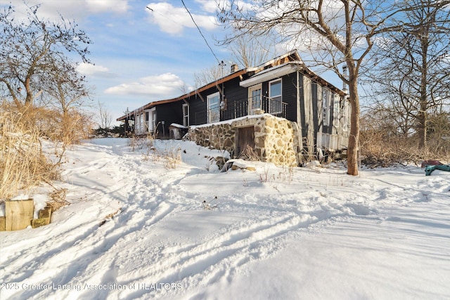 view of snowy exterior featuring stone siding and a balcony