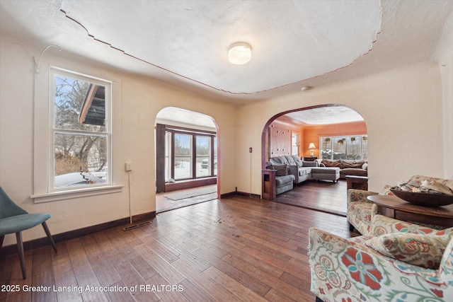 living room featuring a healthy amount of sunlight, baseboards, arched walkways, and dark wood-type flooring