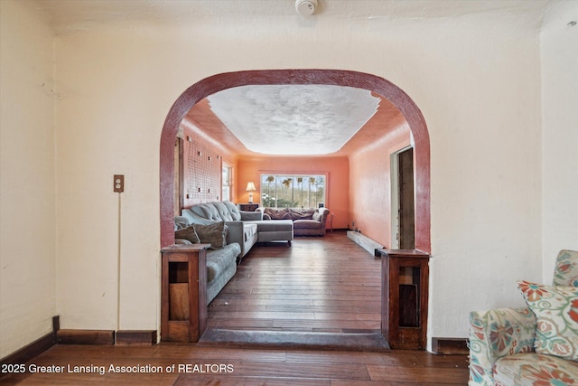 living area featuring dark wood-style floors, baseboards, arched walkways, and a raised ceiling