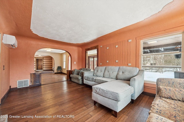 living area featuring dark wood-style floors, baseboards, visible vents, and a wall mounted air conditioner