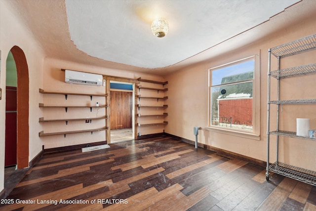 spare room with arched walkways, dark wood-type flooring, a wall mounted air conditioner, and baseboards