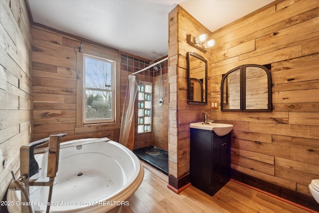 full bathroom featuring a bathing tub, wooden walls, wood finished floors, vanity, and a shower stall