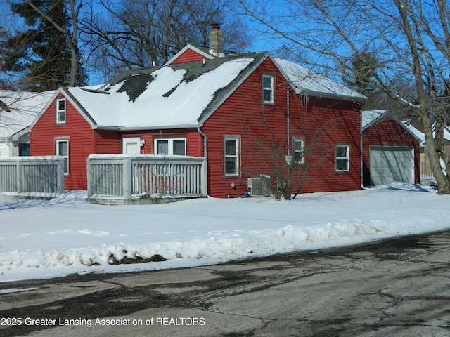 snow covered property with central AC unit, a chimney, and an attached garage