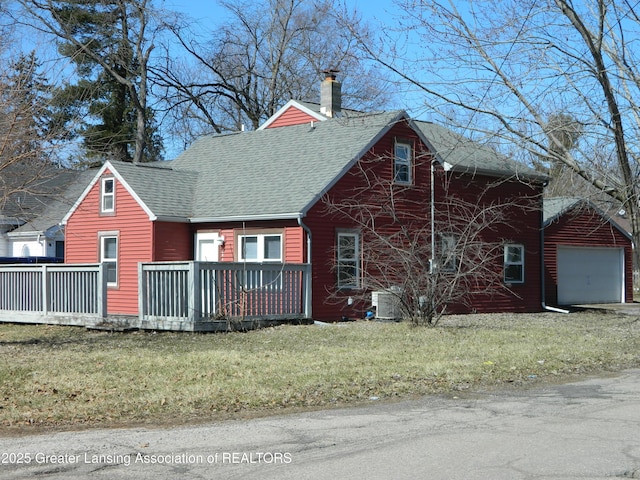 view of front facade featuring a detached garage, a front yard, roof with shingles, and a chimney