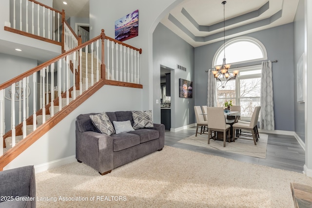 living room with visible vents, a towering ceiling, an inviting chandelier, baseboards, and stairs