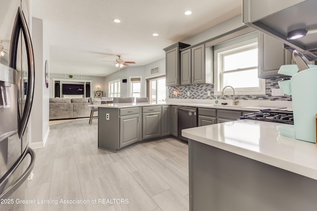 kitchen featuring gray cabinetry, stainless steel appliances, a peninsula, open floor plan, and light countertops