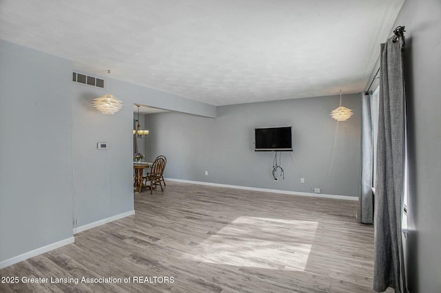 unfurnished living room with an inviting chandelier, light wood-type flooring, visible vents, and baseboards