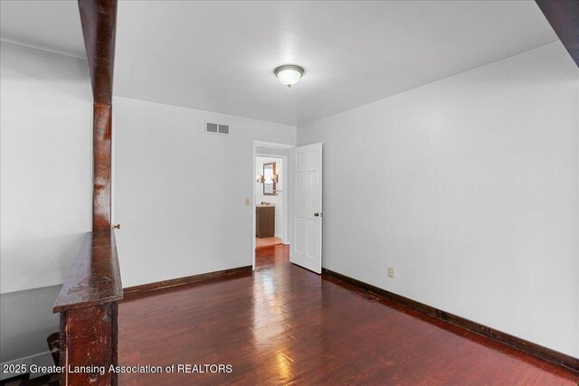 spare room featuring dark wood-style flooring, visible vents, and baseboards