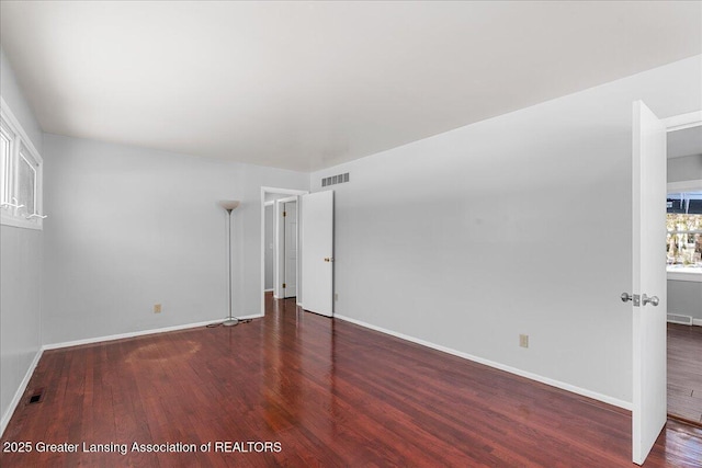 empty room featuring dark wood-style floors, visible vents, and baseboards