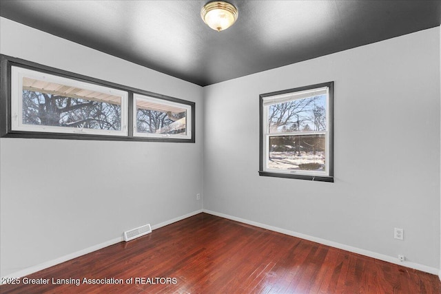 empty room with wood finished floors, visible vents, and baseboards