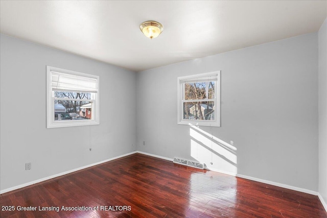 empty room with plenty of natural light, visible vents, baseboards, and wood finished floors