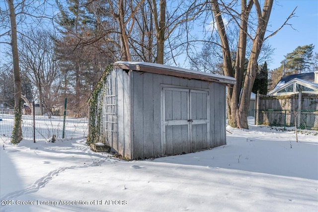 snow covered structure featuring a shed, an outdoor structure, and fence