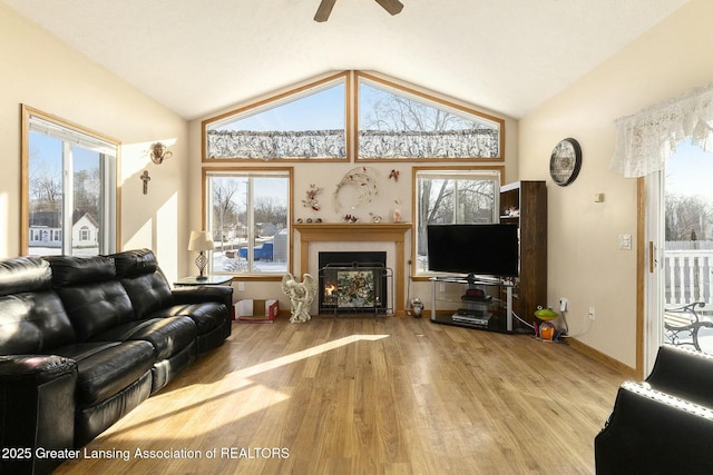 living area featuring a warm lit fireplace, light wood-style flooring, vaulted ceiling, and a wealth of natural light