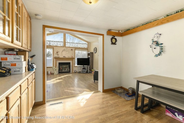 dining room with light wood-type flooring, a fireplace, visible vents, and baseboards