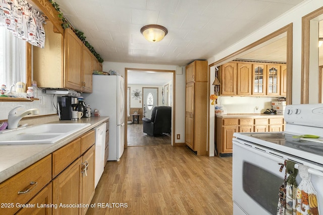 kitchen featuring white appliances, light wood-style flooring, glass insert cabinets, light countertops, and a sink