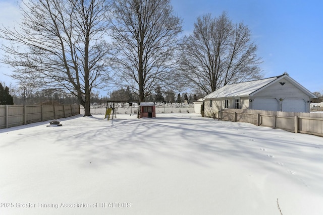 yard layered in snow featuring a garage and fence