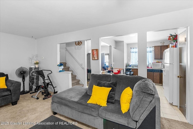 living room featuring light carpet, light tile patterned floors, and stairs