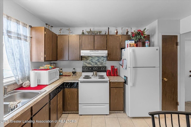 kitchen with under cabinet range hood, white appliances, a sink, light countertops, and plenty of natural light