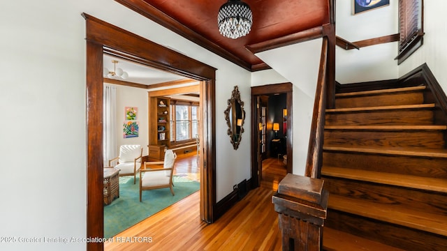 stairway with a chandelier, crown molding, and wood finished floors