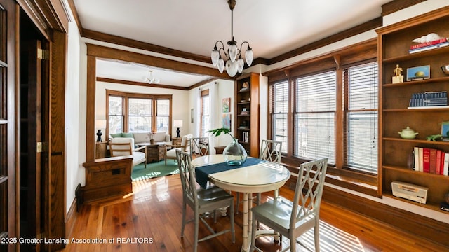 dining space with a chandelier, ornamental molding, and wood finished floors