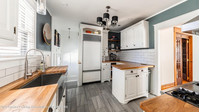 kitchen featuring pendant lighting, open shelves, wooden counters, white cabinets, and a sink