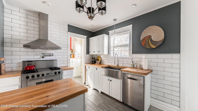 kitchen with white cabinets, wood counters, appliances with stainless steel finishes, wall chimney range hood, and pendant lighting