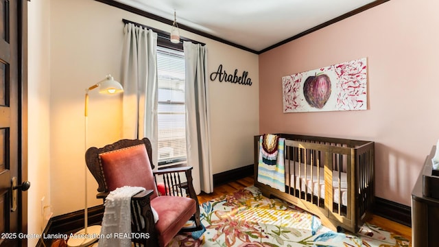 bedroom with a nursery area, baseboards, crown molding, and wood finished floors