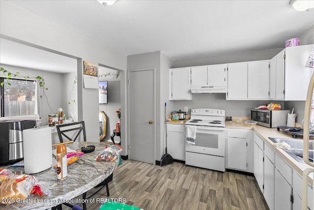 kitchen with under cabinet range hood, electric range, white cabinetry, light countertops, and stainless steel microwave