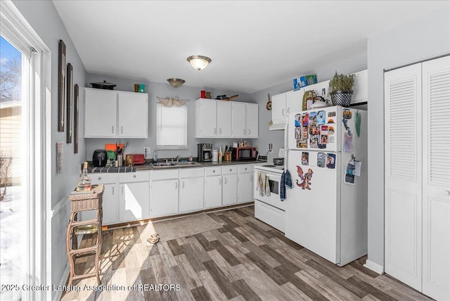 kitchen with dark wood finished floors, dark countertops, white cabinets, a sink, and white appliances