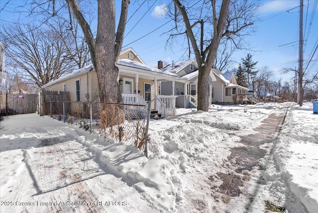 snow covered property featuring covered porch, a chimney, and fence