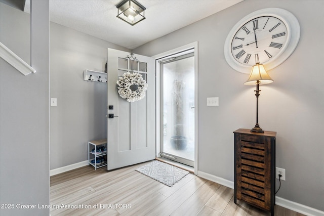 foyer entrance featuring light wood-style floors, baseboards, and a textured ceiling