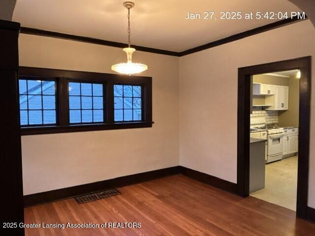 empty room featuring ornamental molding, wood finished floors, visible vents, and baseboards