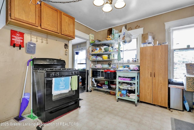 kitchen with light floors, black range with gas cooktop, brown cabinetry, and a wealth of natural light