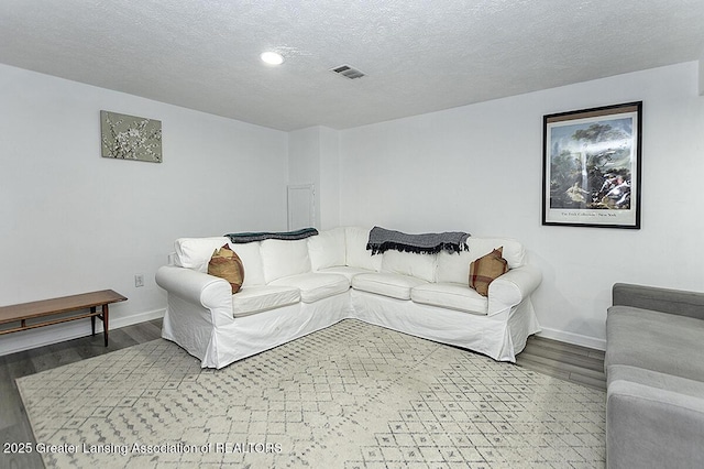 living area with baseboards, a textured ceiling, visible vents, and wood finished floors