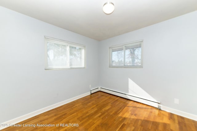 spare room featuring baseboards, a baseboard heating unit, and wood finished floors