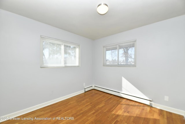 spare room with a baseboard radiator, wood finished floors, and baseboards